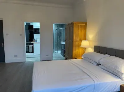 a bedroom with a large white bed and a kitchen at Premier Studio B in Broxburn