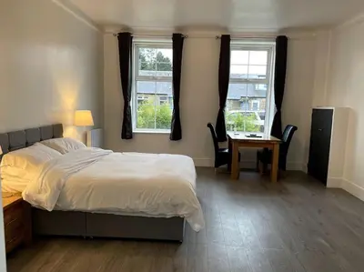 a bedroom with a bed and a desk and two windows at Premier Studio B in Broxburn