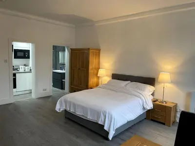 a bedroom with a large bed and a kitchen at Premier Studio B in Broxburn