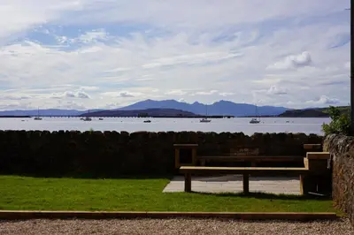 a bench sitting on the grass near a body of water at Beach house no2 with amazing sea views and private garden onto beach. in Fairlie
