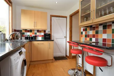 a kitchen with a washing machine and red stools at Freeland Cottage in Dunoon