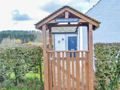 a wooden out house with a gate in a field at Broomlands Cottage in Beattock
