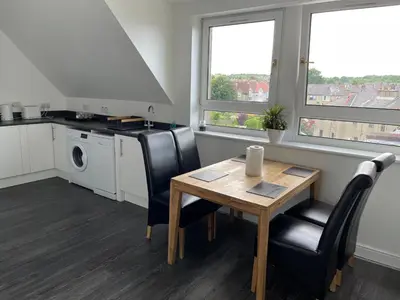 a kitchen with a wooden table and chairs and a table and a sink at Premier Apartment D in Broxburn