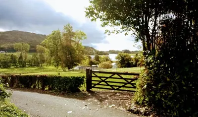 a wooden gate on a road next to a field at Granite Croft in Appin