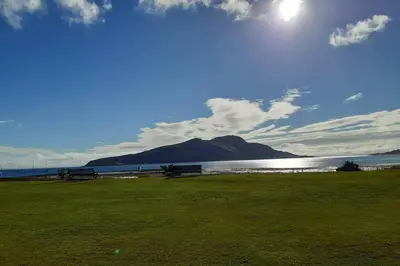 two benches sitting in a field next to a body of water at Cosy cottage with sea views close to local shops. in Lamlash