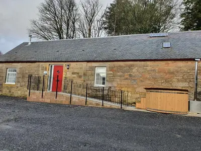 a brick building with a red door on a street at 2-Bed Barn Hot Tub & Pet Friendly near Muirkirk in Cumnock