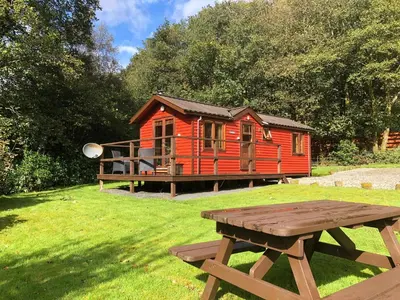 a red cabin with a picnic table in front of it at Rashfield Sheilings - Quiet Riverside Lodges for Couples near Pucks Glen in Dunoon