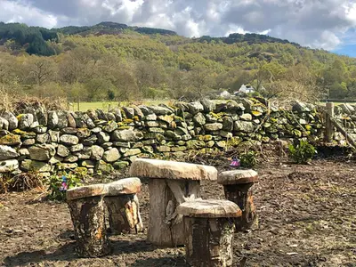 a stone wall and two benches in a field at Clarinnes Cottage in Rowardennan