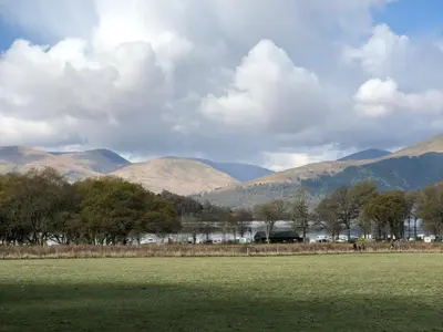 a field with trees and mountains in the background at Clarinnes Cottage in Rowardennan