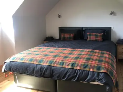 a bedroom with a bed with a plaid blanket at Clarinnes Cottage in Rowardennan
