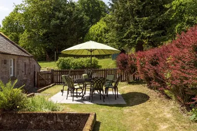 a table and chairs under an umbrella in a yard at Drumlanrig Mains Cottage in Thornhill