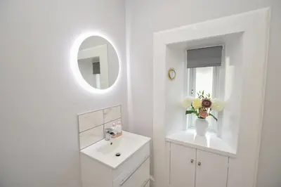 a white bathroom with a sink and a mirror at The Gallery Apartment - Spacious, Town Centre, Walkable to Ferry Terminal, in Oban