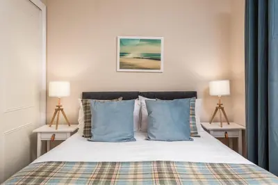 a bedroom with a bed with blue pillows and two lamps at Sunset View - Donnini Apartments in Ayr