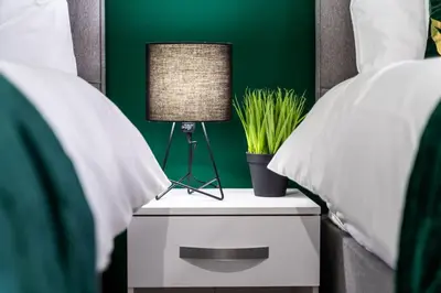 a bedside table with a lamp and a green wall at Cheerful 2 Bedroom Homely Apartment, Sleeps 4 Guest Comfy, 1x Double Bed, 2x Single Beds, Free Parking, Free WiFi, Suitable For Business, Leisure Guest, Contractors, QE Hospital, Glasgow, Near Airport & City Centre, Perfect For Common Wealth Games 2026 in Glasgow