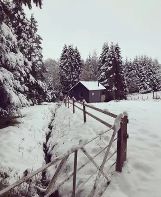 a fence in a snow covered field with a house at The Trossachs Collection in Kepculloch