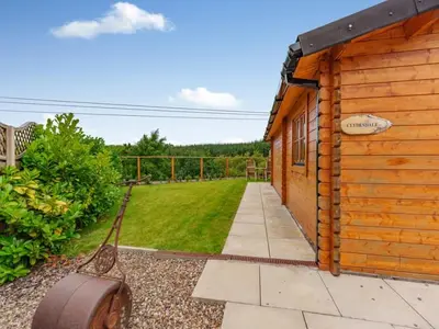 a wooden building with a yard and a lawn at Lochinvar - Clydesdale Log Cabin with Hot Tub in Airdrie