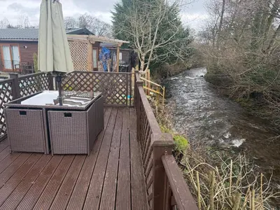 a wooden deck with an umbrella next to a river at Deer lodge in Auchterarder