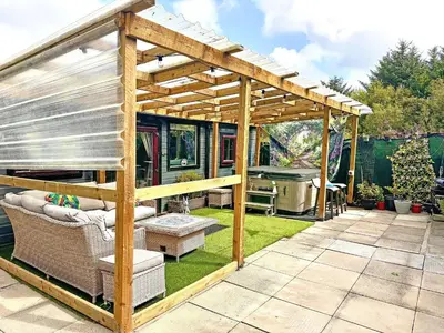 a wooden pergola on a lawn with a grill at Bumbles Barn in Slamannan