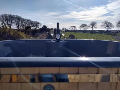 a blue bath tub with a bottle of wine in it at Cleeves Cabins Ailsa Luxury Lodge with hot tub in Dalry
