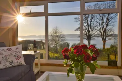 a vase of roses sitting on a table in front of a window at Scallopshell Lodge in Otter Ferry