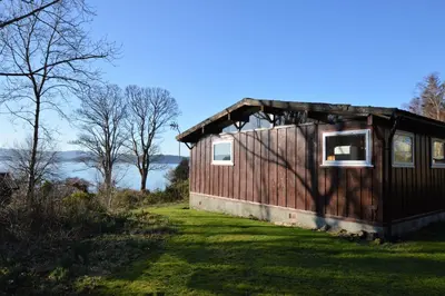 a small wooden building with two windows on a grass field at Scallopshell Lodge in Otter Ferry