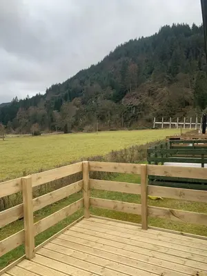 a wooden fence next to a field with a hill at The Castleton Sea View 13 in Dunoon