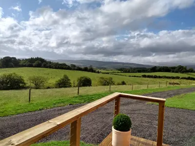 a wooden rail with a potted plant on a porch at Cleeves Cabins Arran Luxury Lodge with hot tub in Dalry