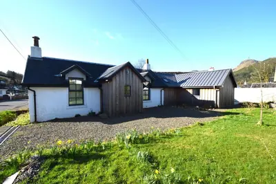 a small white house with a grass yard at Arivean Cottage in Lochgoilhead