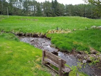 a wooden bench sitting next to a stream at Lazy Days Lodge, Glendevon, Perthshire in Glendevon