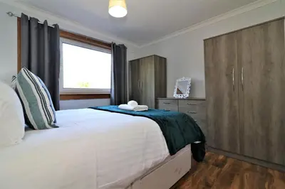 a bedroom with a large white bed with a wooden cabinet at Signature - Dumbreck House in Glasgow
