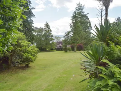 a large grassy yard with trees and bushes at Cluniter Cottage in Innellan