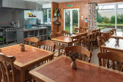 a restaurant with wooden tables and chairs and a kitchen at Inveraray Hostel in Inveraray