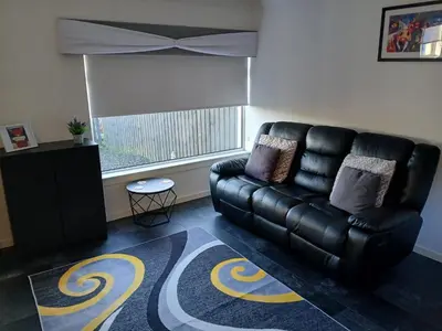 a black leather couch in a living room with a window at The Cottage - Hot Tub - nr Glasgow - self check-in in Coatbridge