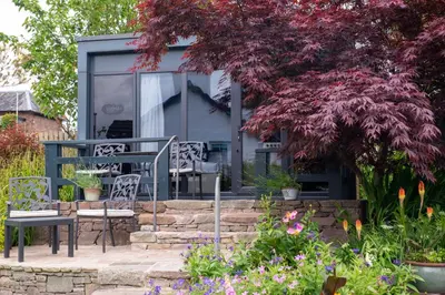 a patio with a table and chairs in a garden at Braeside Guest House, Loch Lomond in Drymen