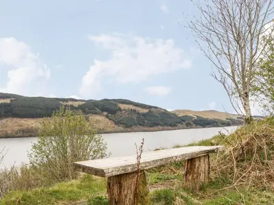 a wooden bench sitting next to a body of water at Innishail in Lochgilphead