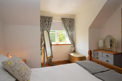 a bedroom with a bed and a window and a mirror at High Beach Cottage in Kames