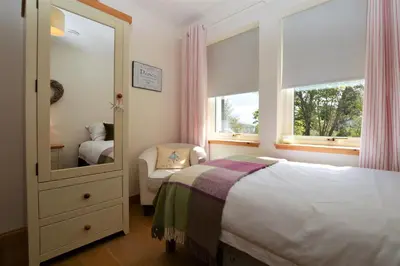 a bedroom with a bed and a mirror and a chair at High Beach Cottage in Kames