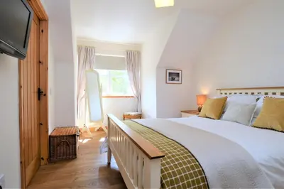 a bedroom with a large bed and a television at High Beach Cottage in Kames