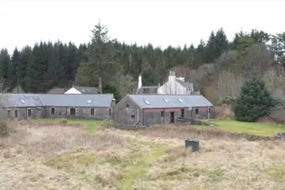 an old barn in a field next to a forest at Maberry Cottage in Bargrennan