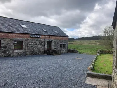 a stone house with a gravel driveway in front of it at Merrick Cottage in Bargrennan