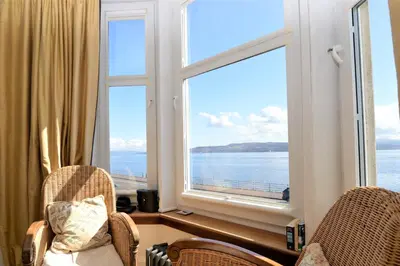 two chairs in front of a window with a view of the ocean at Kimberley Apartment in Dunoon