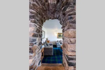 an archway into a living room with a stone wall at Meadowhead Cottage, Traditional Scottish Cottage in Waterside