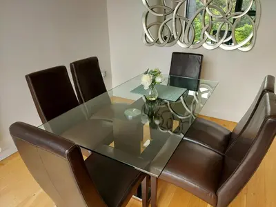 a glass dining room table with leather chairs and a chandelier at Quartermile Luxury Landing Apartment in Edinburgh