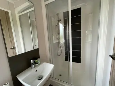 a white bathroom with a shower and a sink at Pirnie Lodge Holiday Lets in Slamannan