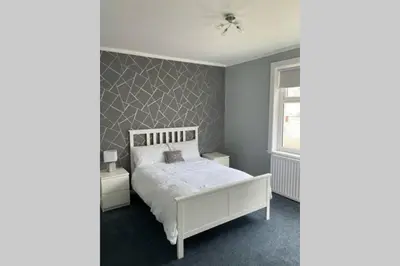 a bedroom with a white bed and a gray wall at Beautiful two bedroom flat by the Loch in Balloch