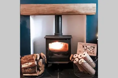 a wood stove in a room with a basket of logs at Glendyne Cottages, Highest Village in Scotland in Wanlockhead