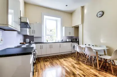 a kitchen with white cabinets and a table and chairs at Stunning 5 bedroom apt, close to city centre, SEC, Hydro and motorway in Glasgow