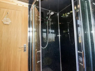 a shower with a glass door next to a wooden cabinet at Blackbrae Cabin in Coatbridge
