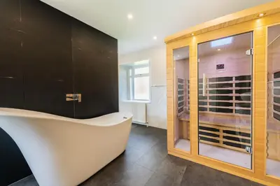 a bathroom with a bath tub and a glass cabinet with wine bottles at Nether Newton - Sleeps 12, Hottub, Sauna, Private Garden in Newmilns