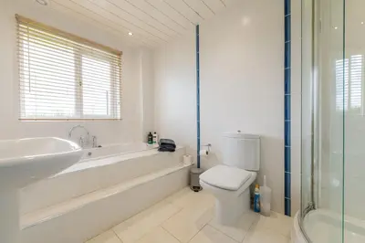 a white bathroom with a tub and a toilet and a sink at Alton Villa, Sleeps 12, Great for Families, Undercover Hotub & Games Room in Newmilns